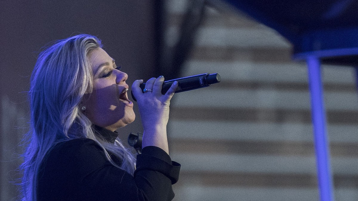 Kelly Clarkson singing into a handheld microphone under blue stage lights