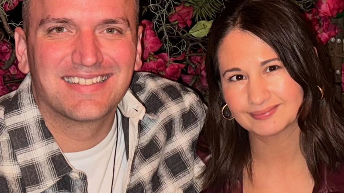 Ken Urker in a plaid flannel shirt smiling next to Gypsy Rose Blanchard in front of pink flowers