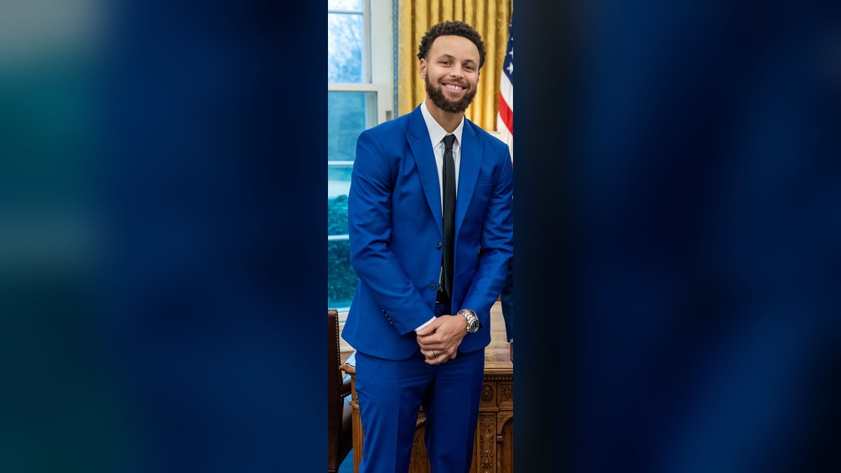 Warriors star Stephen Curry smiles in a blue suit during a 2023 visit to the White House Oval Office
