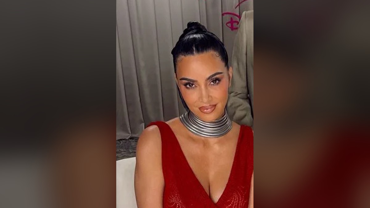 Kim Kardashian in a red dress and silver choker smiling softly at a press event
