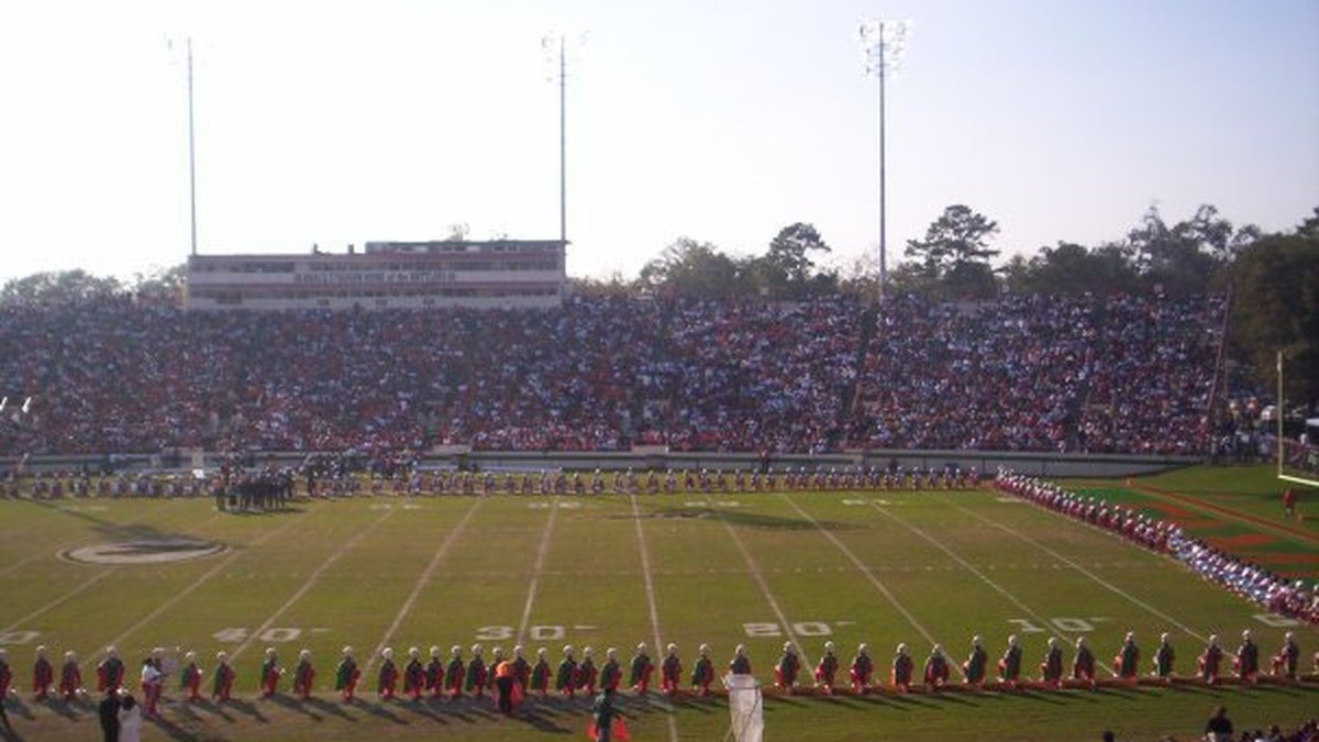 A marching band stands in formation on the field at Bragg Memorial Stadium in front of packed stands