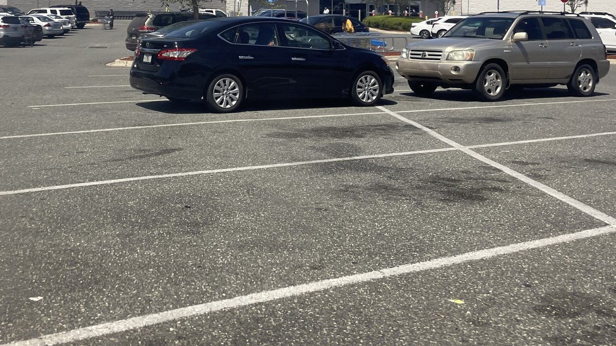 A black sedan and a gold SUV parked in a sunny store parking lot