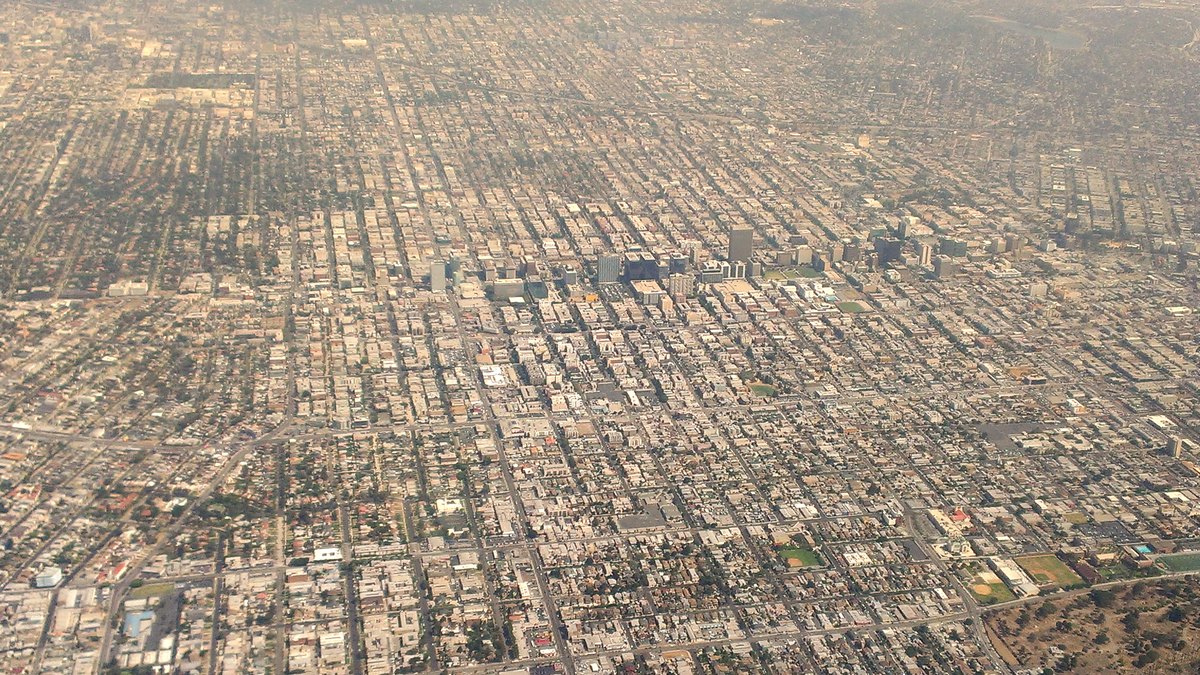 An aerial view looks north over the dense street grid of Koreatown in Los Angeles with mid-rise towers and hills in the distance