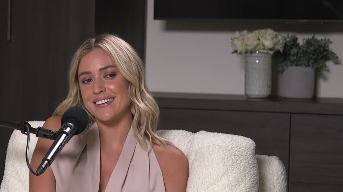 Kristin Cavallari smiling in a beige halter top while sitting at a podcast microphone