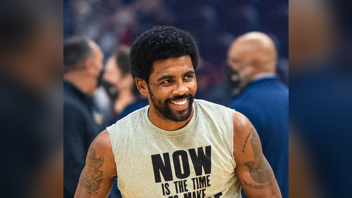 Kyrie Irving smiling in a sleeveless warm-up shirt with a social justice message while holding a basketball before a 2022 game