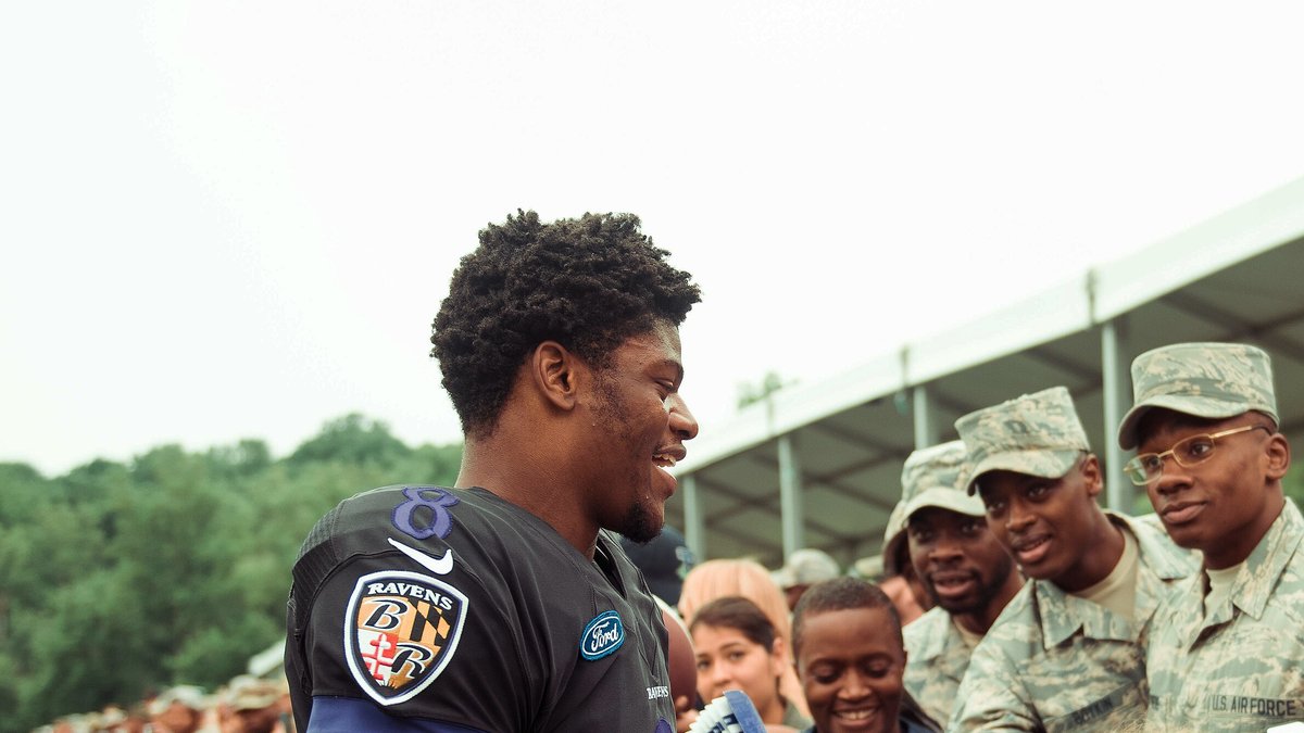 Smiling Baltimore Ravens quarterback Lamar Jackson in a black Ravens practice jersey greets service members at training camp