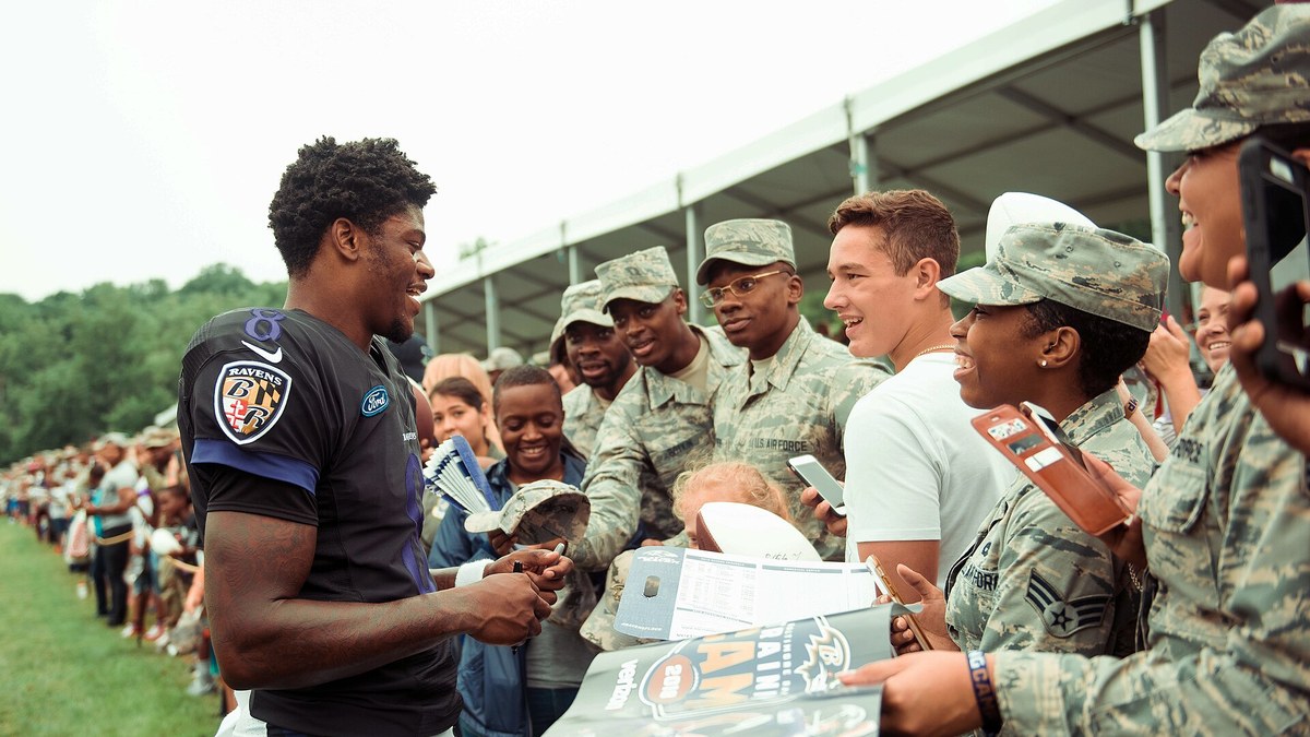 Lamar Jackson smiling as he signs autographs in a black Baltimore Ravens jersey