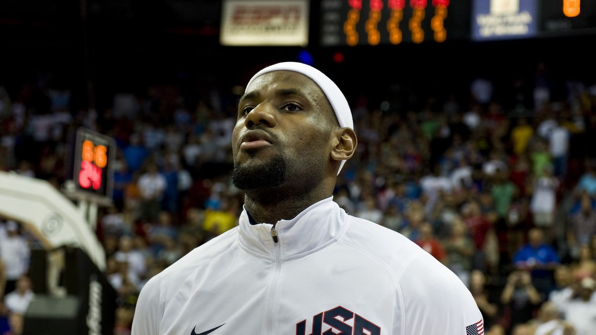 LeBron James in a white Team USA warmup jacket and headband stands for the national anthem before a game