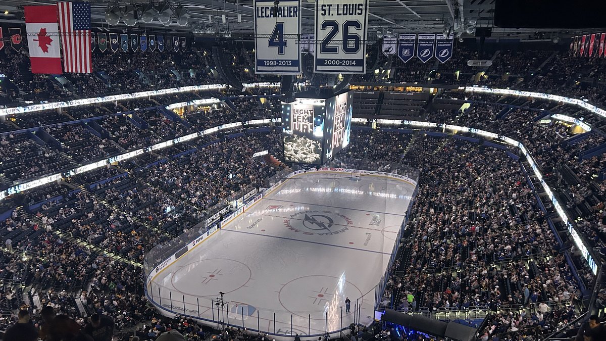 A packed crowd fills the Tampa Bay Lightning's home arena before a game with retired jerseys hanging above the ice