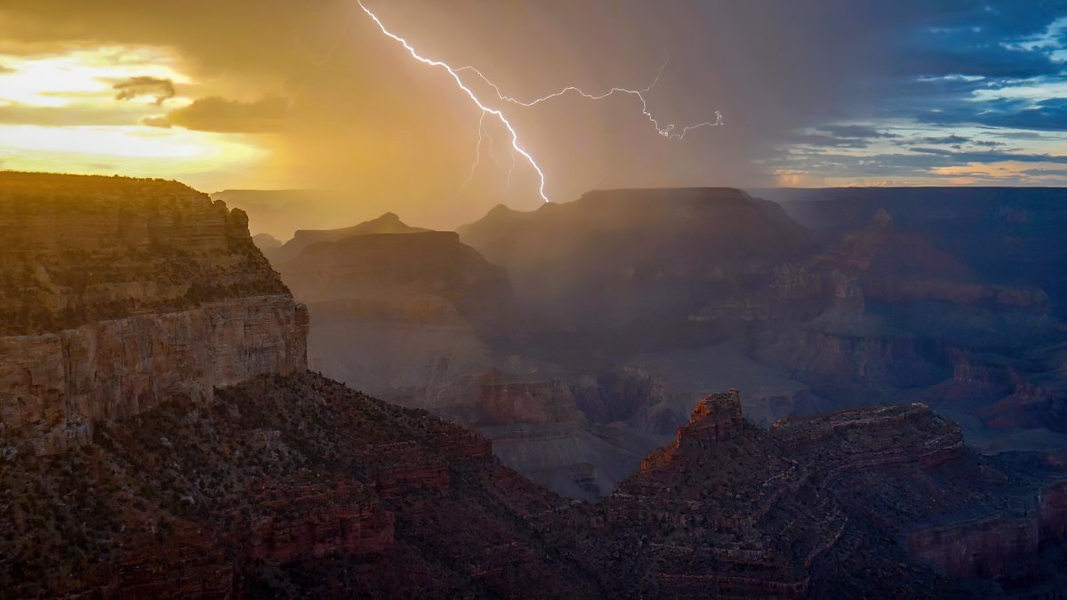 A lightning bolt strikes from dark storm clouds over the rocky cliffs of the Grand Canyon in northern Arizona at sunset