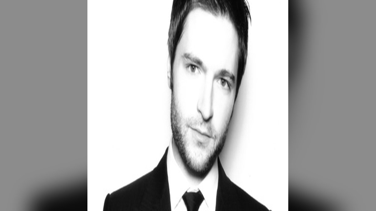 Lucian Piane in a black-and-white portrait wearing a dark suit and tie