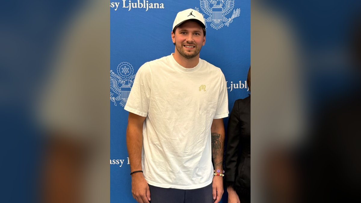 Luka Dončić smiles in a white T-shirt and white cap at the U.S. Embassy in Ljubljana in August 2026