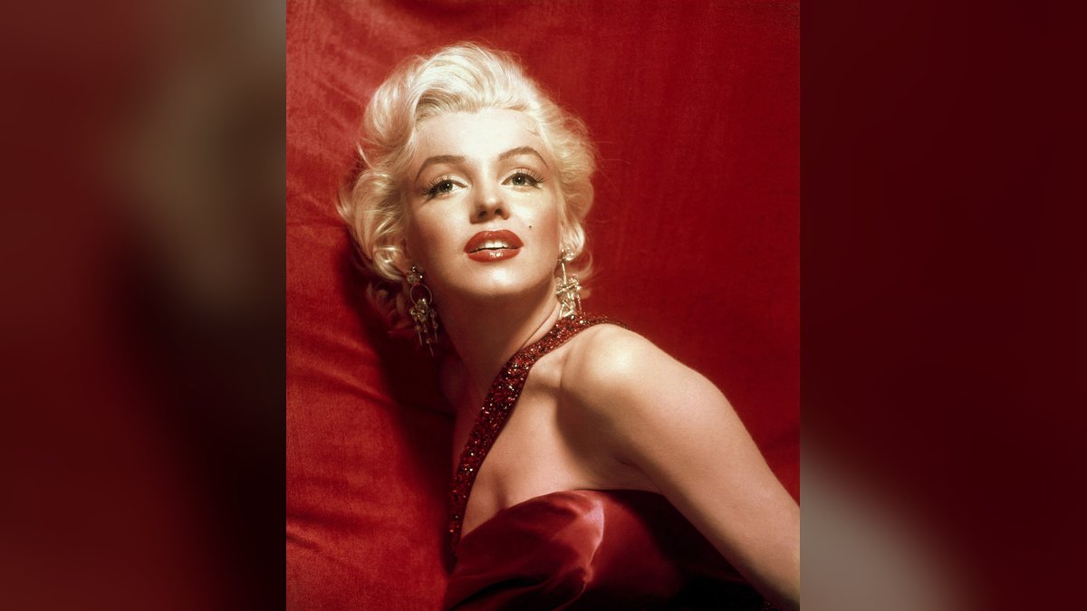 Marilyn Monroe in a red satin gown with diamond earrings against a red backdrop