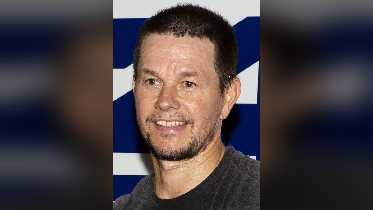 Mark Wahlberg in a dark crew-neck shirt smiling at a Marine Corps event