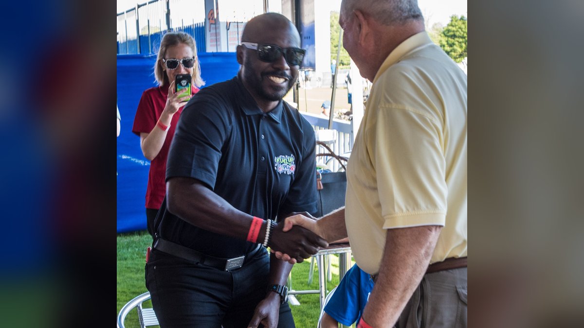 Marshall Faulk smiling in sunglasses as he shakes hands with a guest at a youth fitness event at Indianapolis Colts training camp in 2017