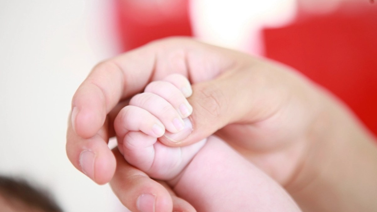 An adult hand gently holding a newborn baby's tiny fist