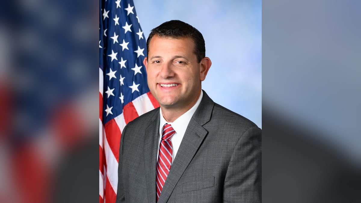 Rep. David Valadao smiles in a gray suit and striped red tie in his official congressional portrait beside an American flag