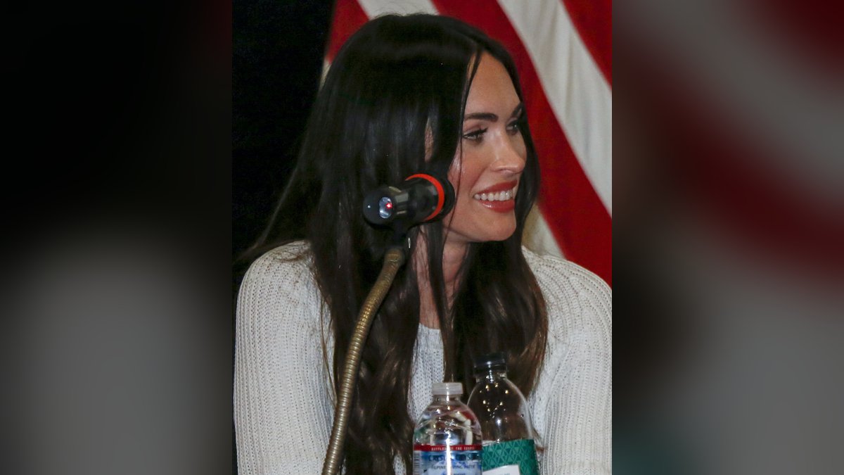 Megan Fox smiling at a microphone during a 2019 visit with US troops