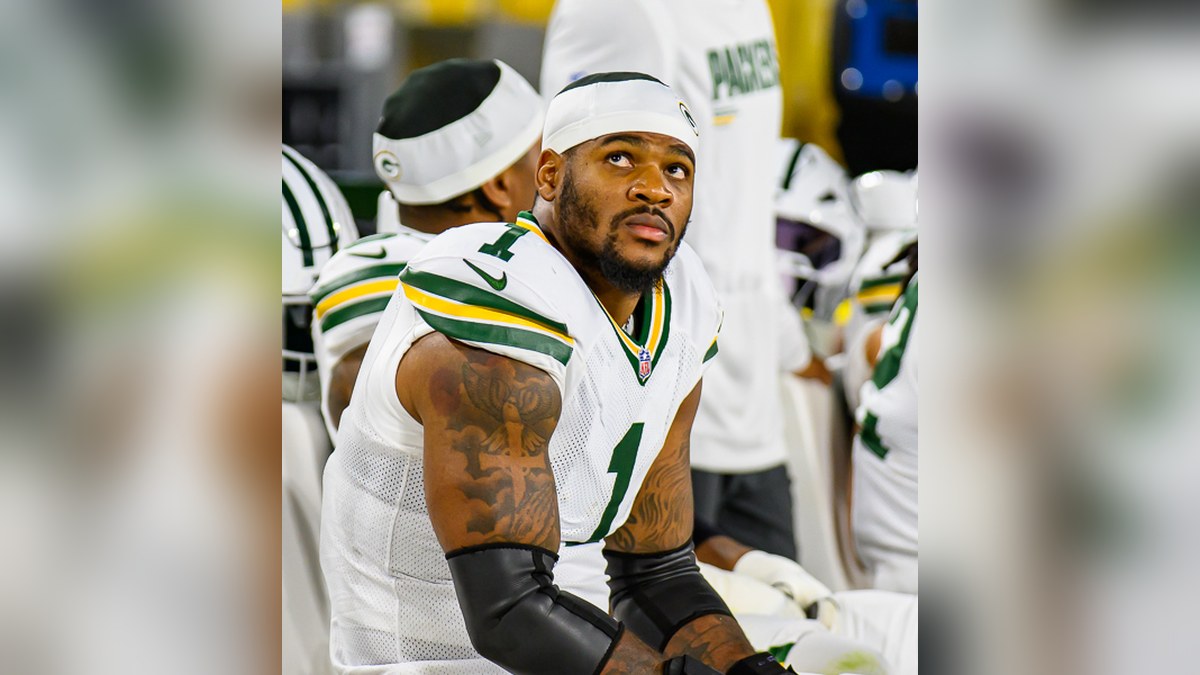 Micah Parsons in a white Packers No. 1 jersey and headband looking up from the sideline bench