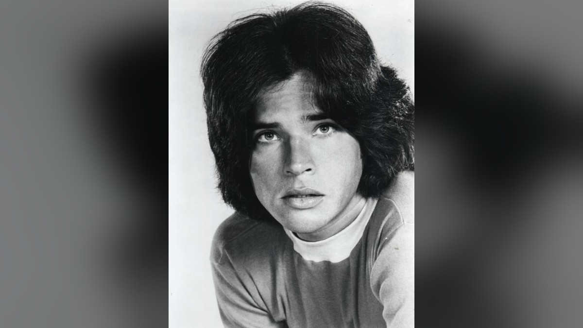 Black and white 1970s portrait of a young Michael Gray with thick shoulder-length hair