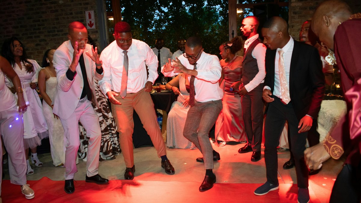 Young Black men in shirts and ties dancing on a red carpet at a festive formal party