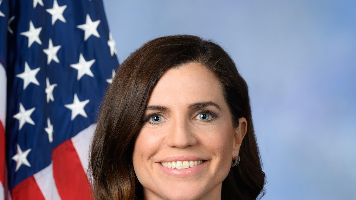 Rep. Nancy Mace smiling in a navy dress in her official portrait in front of an American flag