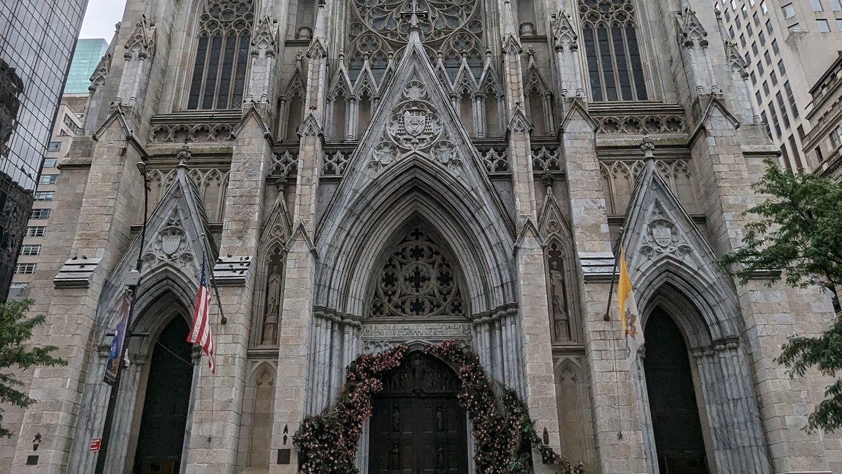 The gray stone Gothic front of St. Patrick's Cathedral in Manhattan with its rose window, carved arches and a flower-framed bronze door