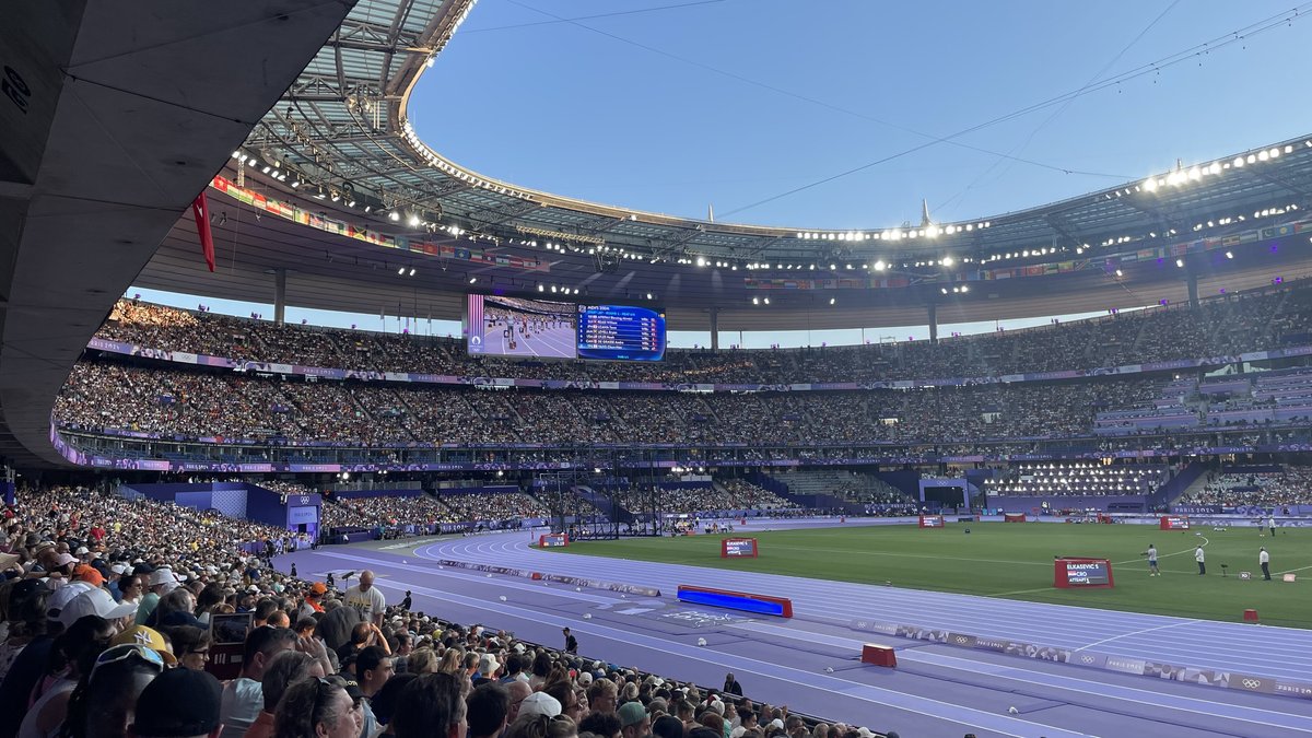 Packed stands under the curved roof of Stade de France in Saint-Denis on a sunny evening during the 2024 Olympics