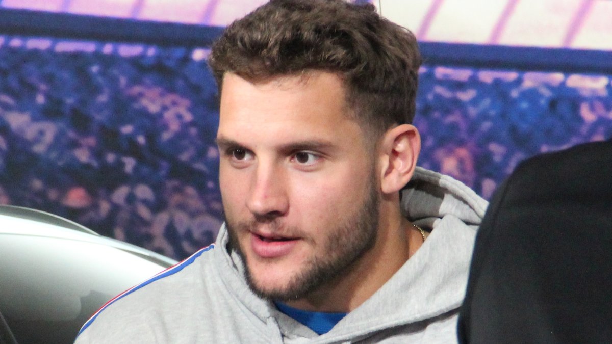 Nick Bosa in a gray hoodie sits at a table with a signed football and a blue and red helmet