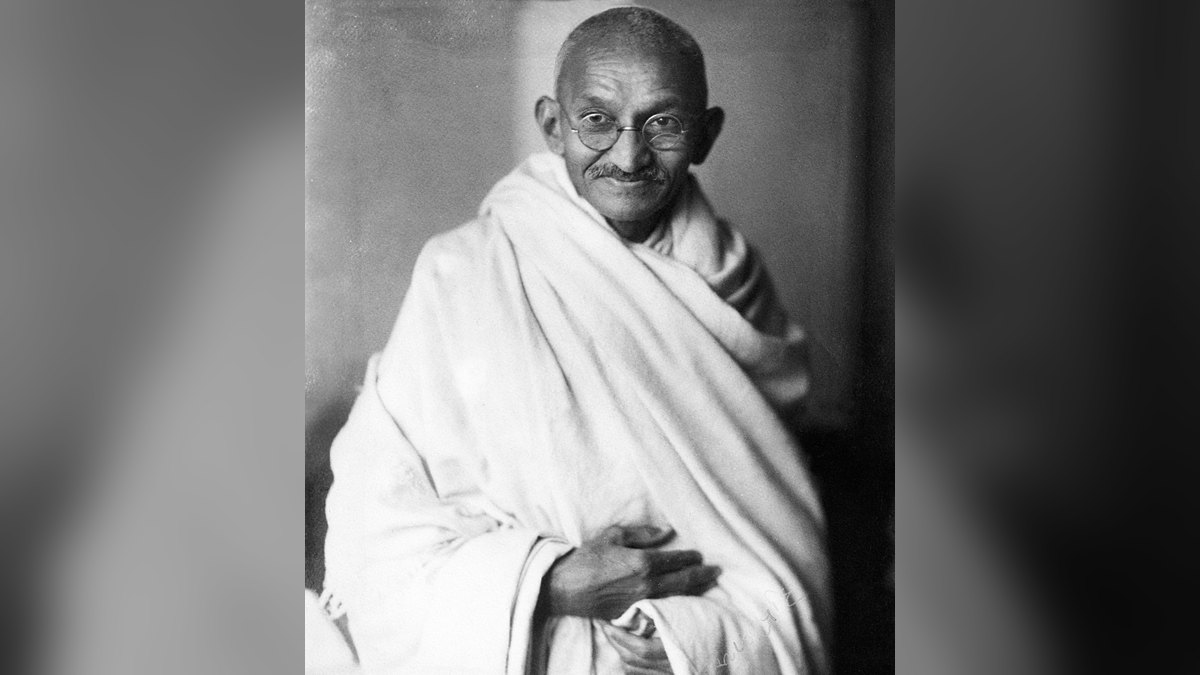 Mahatma Gandhi smiling in a white shawl in a 1931 black and white studio portrait