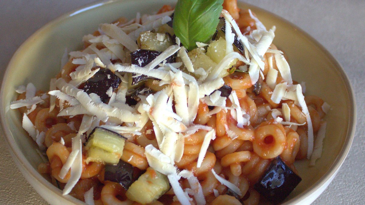 A bowl of pasta topped with basil and shaved cheese sits on a gray table