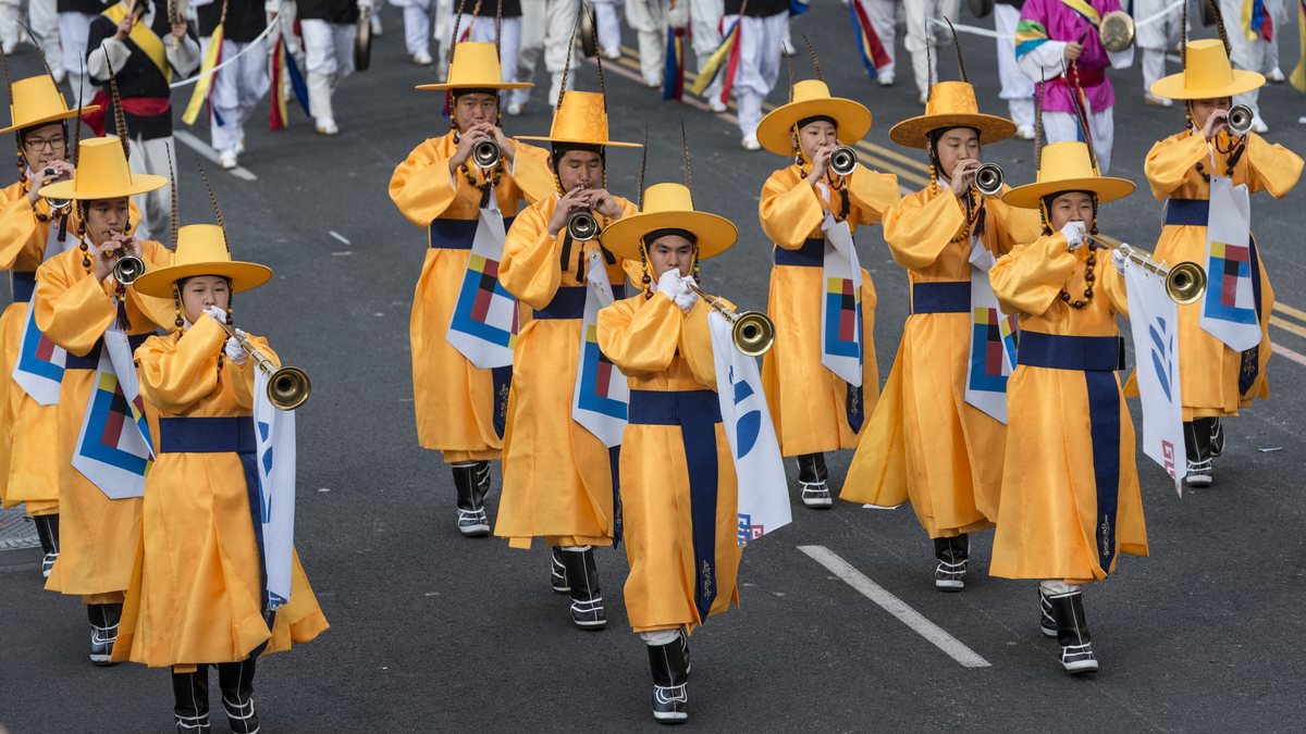Marchers in yellow traditional Korean robes and hats playing brass instruments in a parade
