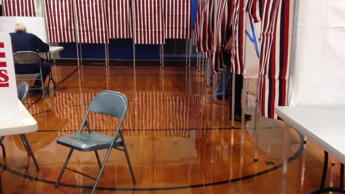 Voting booths with striped curtains set up inside a school gym used as a polling place