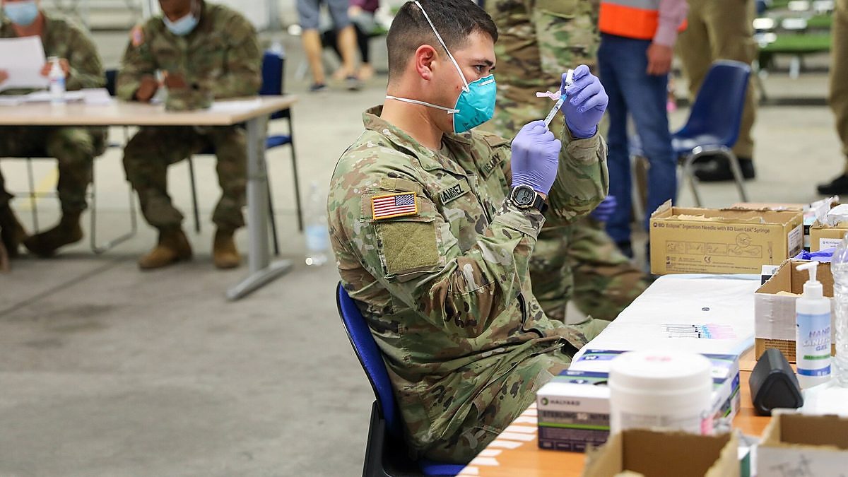 A medical worker in gloves and a mask prepares doses of measles vaccine at a clinic table