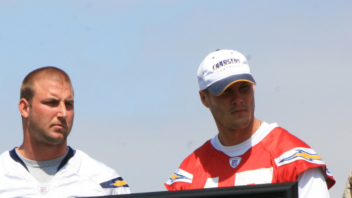 Philip Rivers in a Chargers cap and red Chargers jersey standing next to center Nick Hardwick at an outdoor team event
