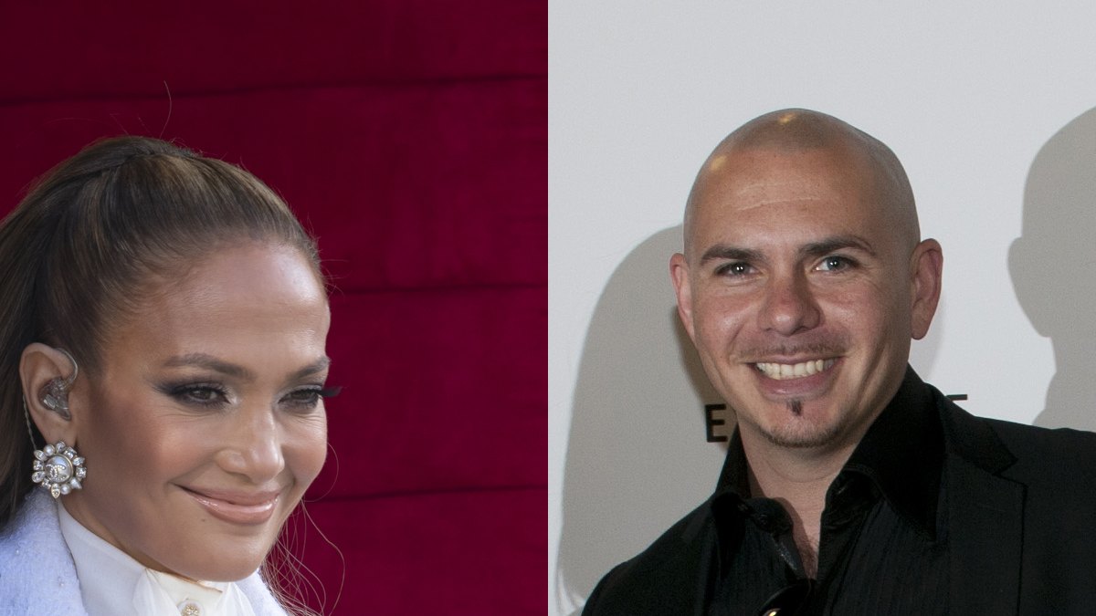 Jennifer Lopez smiling in a white coat beside Pitbull smiling in a black shirt and jacket