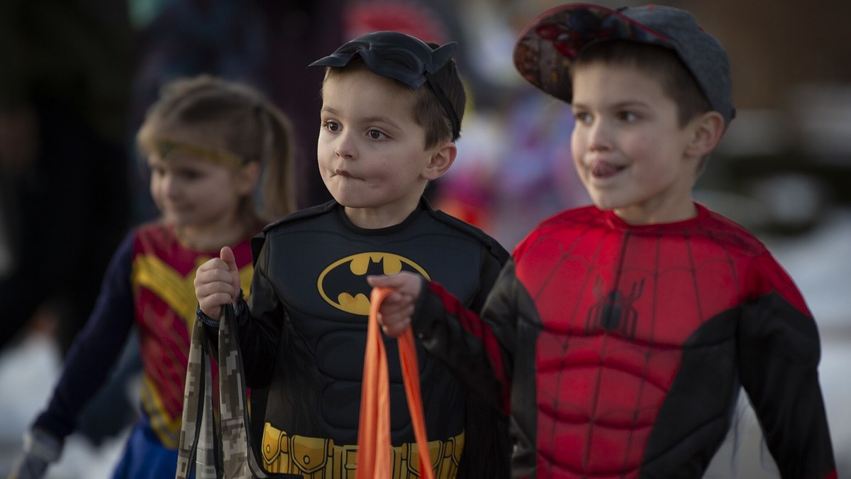 Young children dressed as Batman, Spider-Man and Wonder Woman carry trick-or-treat bags at a Halloween parade