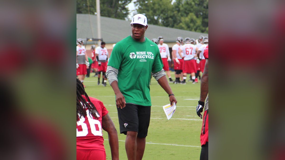 Raheem Morris in a green shirt and white cap coaching defensive backs on the field at Atlanta Falcons training camp
