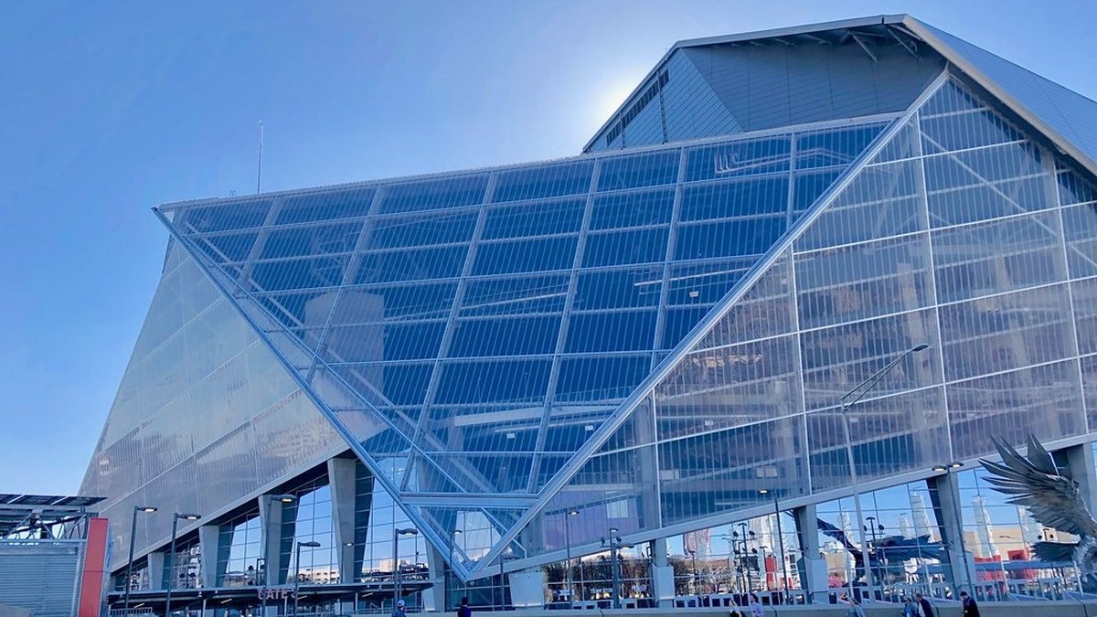 The glass and steel exterior of Mercedes-Benz Stadium in Atlanta under a clear blue sky