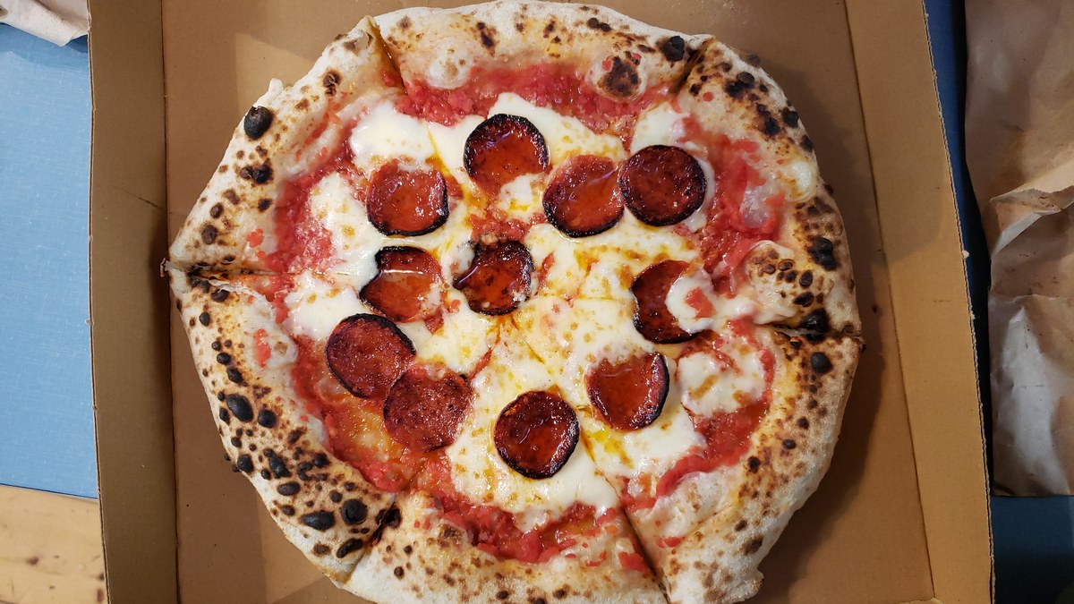 A pepperoni pizza with a blistered golden crust and melted mozzarella sitting in an open cardboard box