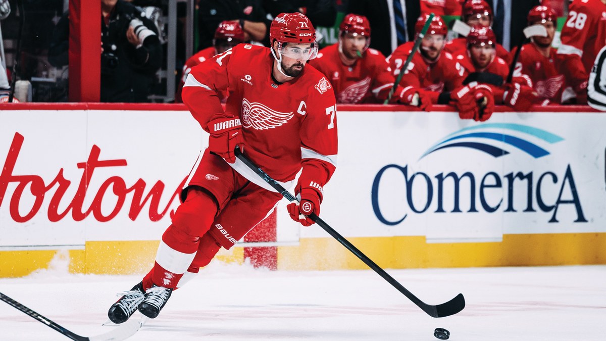 Dylan Larkin skating with the puck in a red Detroit Red Wings jersey
