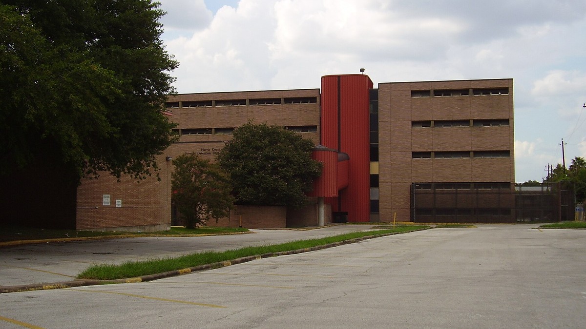 The brick Harris County Juvenile Detention Center in Houston with a red stair tower and an empty parking lot under a cloudy sky