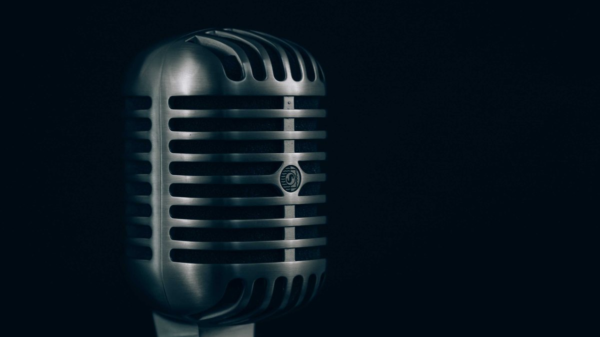 A classic chrome vintage microphone glows under a soft light against a dark background