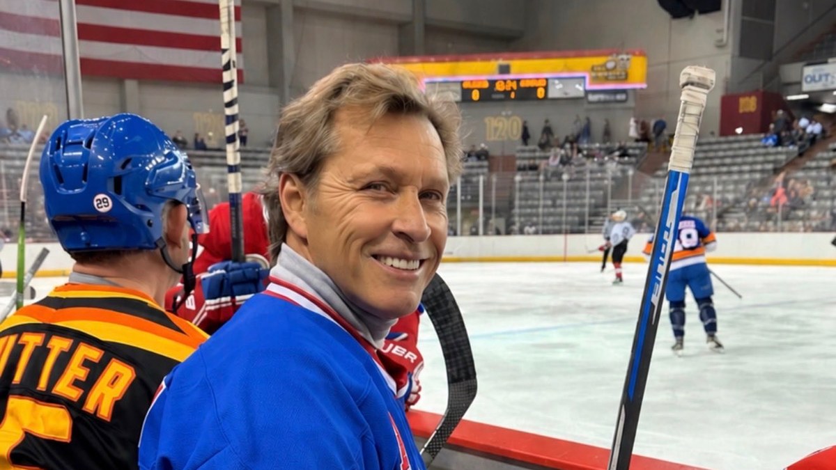 Ron Duguay smiling on a rink bench in a blue number 10 Rangers jersey