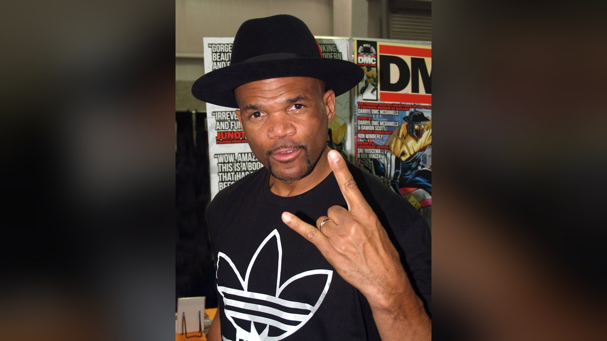 Darryl McDaniels of Run-DMC in a black hat flashing a rock hand sign at a comic convention