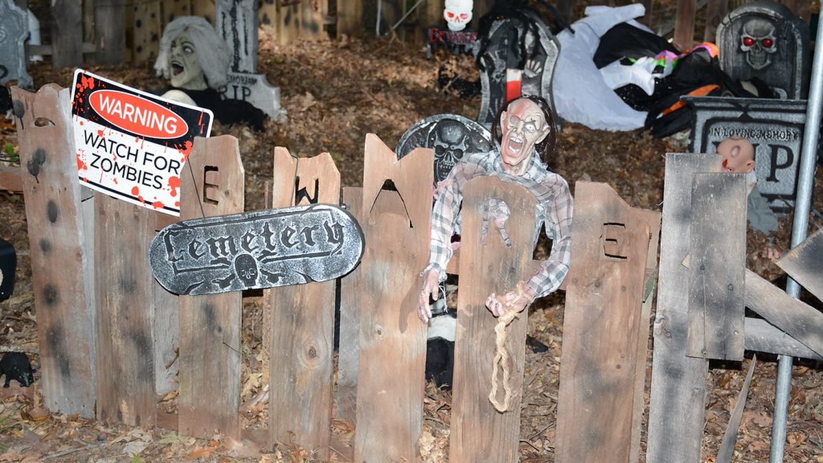 Outdoor Halloween cemetery display with a zombie prop clinging to a wooden Beware fence