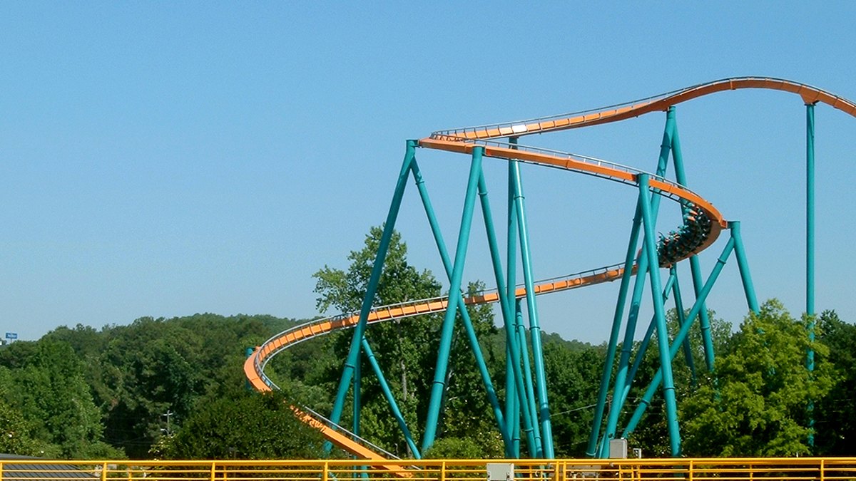 Orange track and teal steel supports of the Goliath roller coaster curving above green trees at Six Flags Over Georgia