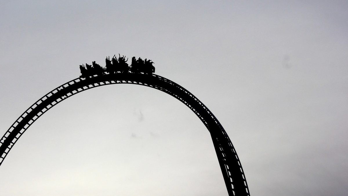 Silhouette of a roller coaster train cresting a steep arched track under a pale sky