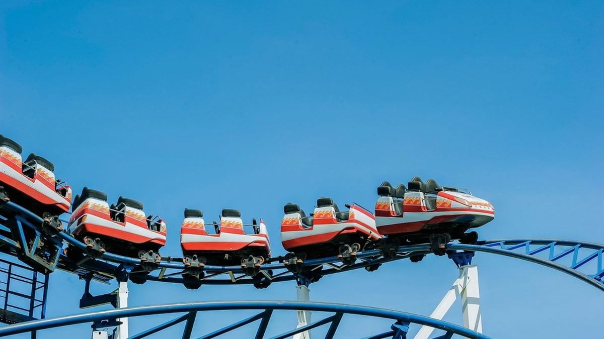 A red roller coaster train rounding a curve on a blue steel track under a clear sky