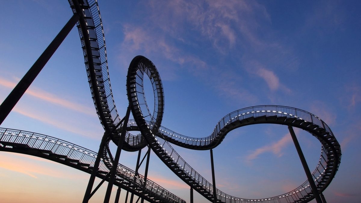 A twisting steel track sculpture shaped like a roller coaster against a pink and blue dusk sky